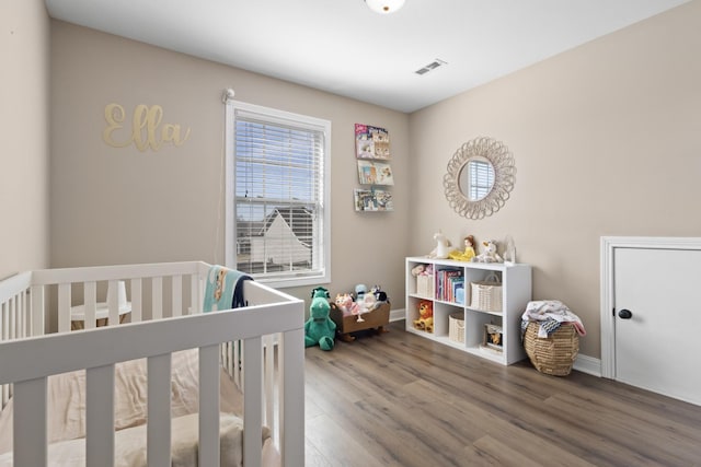 bedroom featuring a nursery area, baseboards, visible vents, and wood finished floors