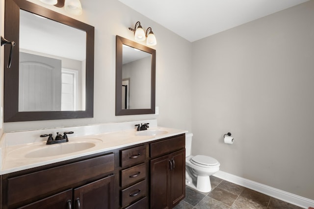 full bath with double vanity, a sink, toilet, and baseboards