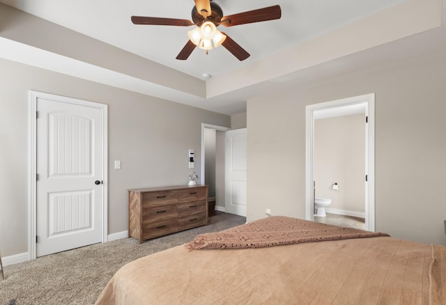 bedroom featuring carpet flooring, a ceiling fan, baseboards, a tray ceiling, and ensuite bath