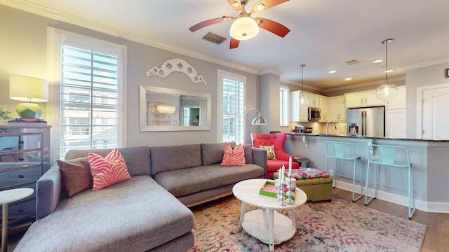 living room with light wood finished floors, visible vents, ornamental molding, and ceiling fan