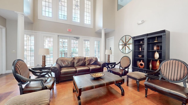 living area with light tile patterned floors, french doors, a towering ceiling, and ornate columns