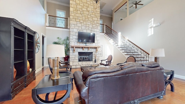 living room featuring a stone fireplace, a high ceiling, baseboards, ornamental molding, and stairway