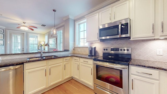 kitchen featuring stainless steel appliances, a sink, decorative backsplash, dark stone countertops, and crown molding