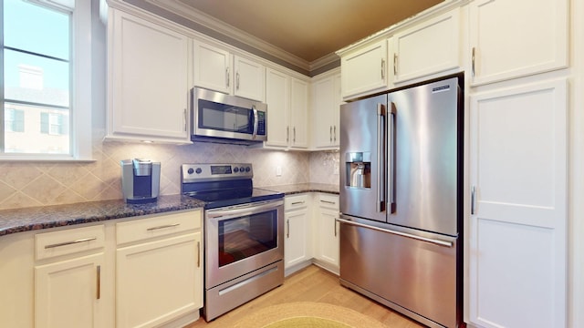 kitchen with stainless steel appliances, light wood-style floors, white cabinets, tasteful backsplash, and dark stone countertops