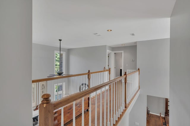 hall featuring baseboards, visible vents, an upstairs landing, and wood finished floors