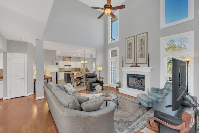 living area with ceiling fan, plenty of natural light, a fireplace with raised hearth, and wood finished floors