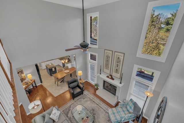 living room featuring a fireplace with raised hearth, a high ceiling, a ceiling fan, wood finished floors, and baseboards