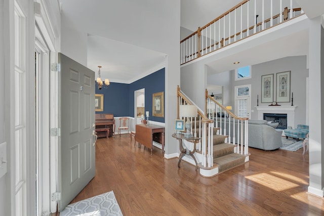 foyer entrance featuring a glass covered fireplace, a towering ceiling, stairway, wood finished floors, and a chandelier