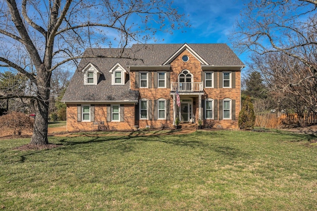 view of front facade featuring a balcony, a shingled roof, a front lawn, and brick siding