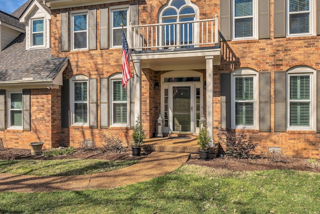 view of exterior entry featuring roof with shingles, brick siding, and crawl space