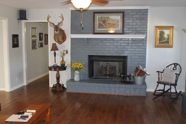 living area featuring a fireplace, dark wood finished floors, a ceiling fan, and baseboards