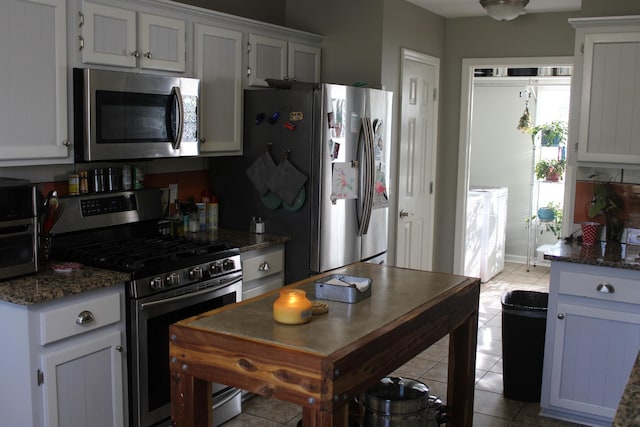 kitchen with dark stone counters, stainless steel appliances, light tile patterned flooring, and white cabinets