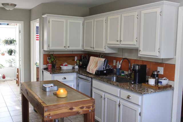 kitchen with dark stone counters, white cabinets, stainless steel dishwasher, a sink, and light tile patterned flooring