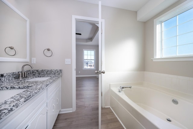 bathroom with a garden tub, vanity, baseboards, and wood finished floors