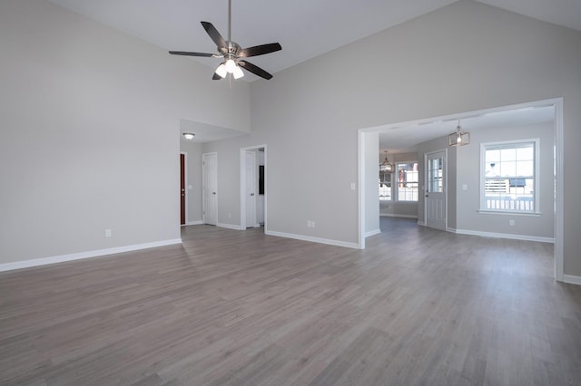 unfurnished living room with ceiling fan, high vaulted ceiling, wood finished floors, and baseboards