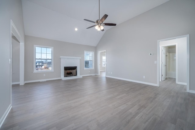 unfurnished living room with high vaulted ceiling, wood finished floors, a ceiling fan, baseboards, and a brick fireplace