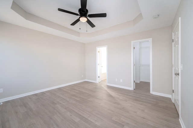 unfurnished bedroom featuring light wood-style floors, baseboards, and a tray ceiling