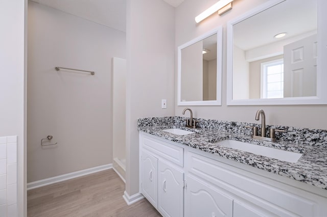 bathroom featuring double vanity, a sink, baseboards, and wood finished floors