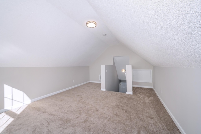 additional living space featuring a textured ceiling, vaulted ceiling, light carpet, and baseboards