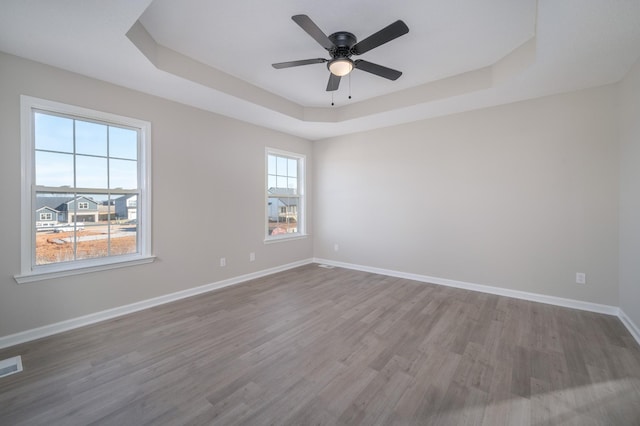 spare room featuring a tray ceiling, visible vents, ceiling fan, wood finished floors, and baseboards