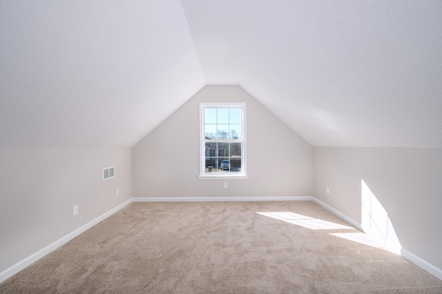 bonus room featuring a textured ceiling, light carpet, visible vents, baseboards, and vaulted ceiling