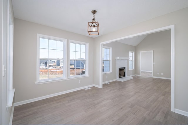 unfurnished living room featuring light wood-style flooring, a fireplace, visible vents, baseboards, and vaulted ceiling