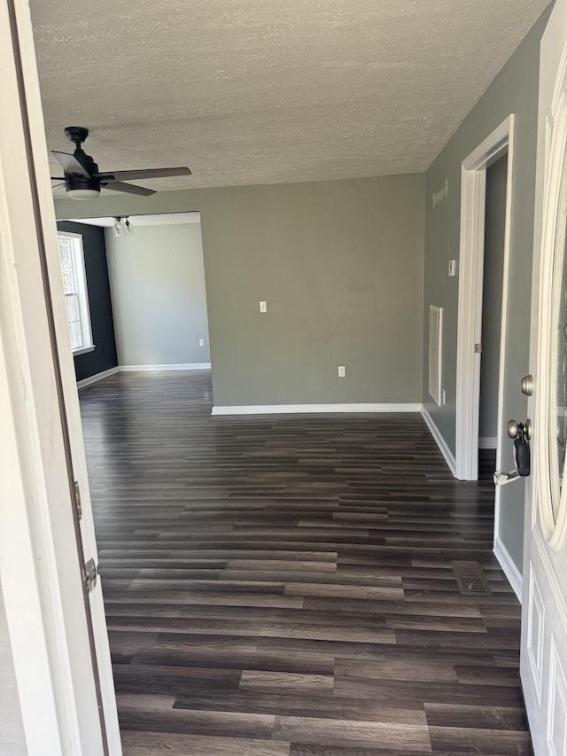 empty room with dark wood-style floors, a textured ceiling, baseboards, and a ceiling fan