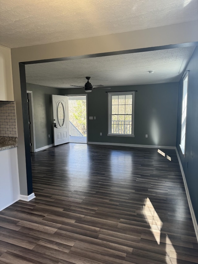 unfurnished living room with baseboards, dark wood-type flooring, a ceiling fan, and a textured ceiling