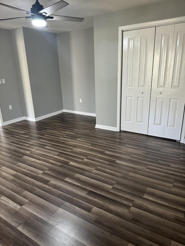 unfurnished bedroom with dark wood finished floors, baseboards, a closet, and ceiling fan