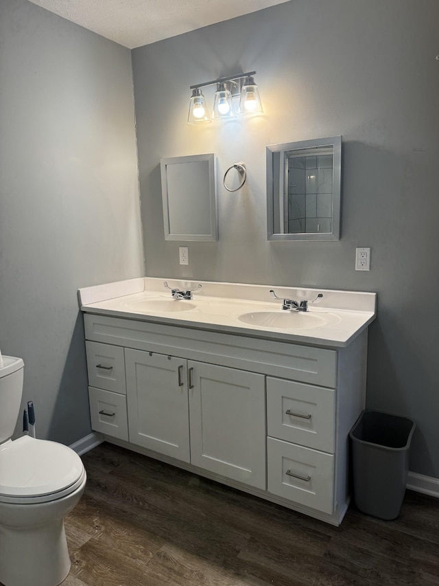 bathroom featuring double vanity, toilet, wood finished floors, and a sink