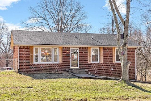 view of front facade featuring roof with shingles, a front yard, and brick siding