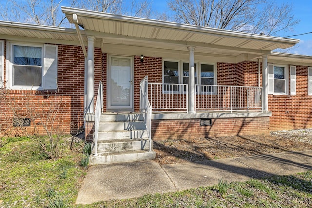 view of exterior entry with crawl space, brick siding, and covered porch