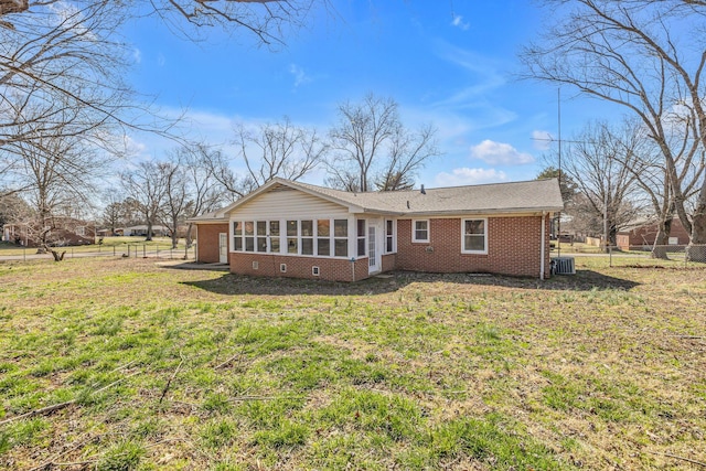 rear view of property with a yard, a sunroom, brick siding, and fence