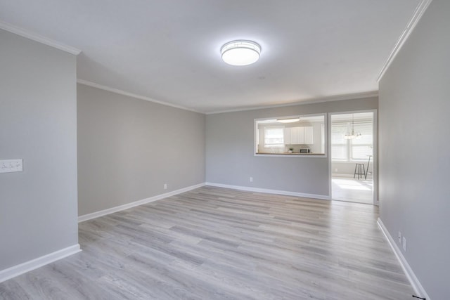 empty room featuring crown molding, light wood finished floors, and baseboards