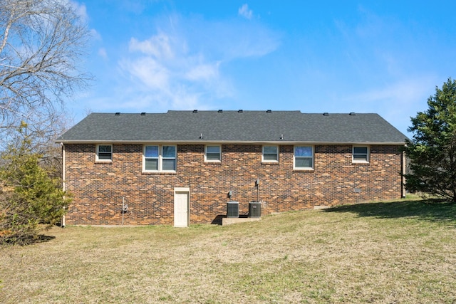 rear view of property featuring brick siding, a lawn, central AC unit, and a shingled roof