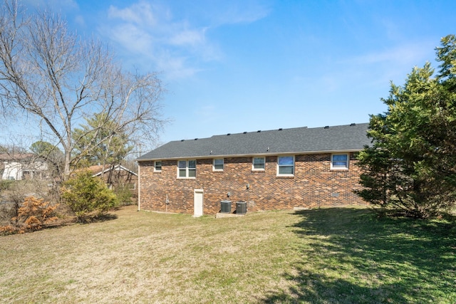 rear view of house featuring a shingled roof, central AC, a yard, and brick siding