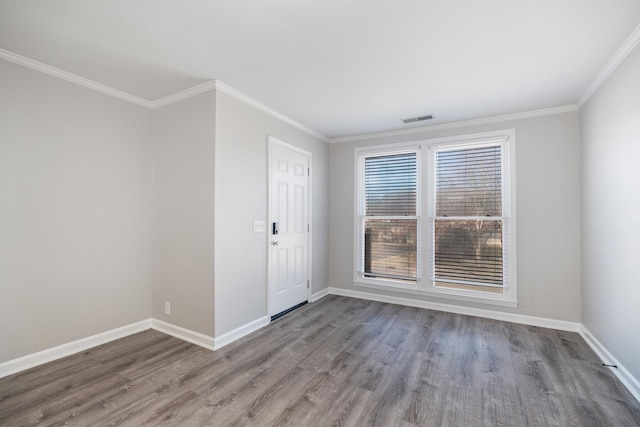 empty room featuring visible vents, crown molding, baseboards, and wood finished floors