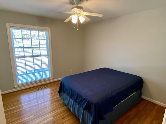 bedroom featuring a ceiling fan, baseboards, visible vents, and wood finished floors