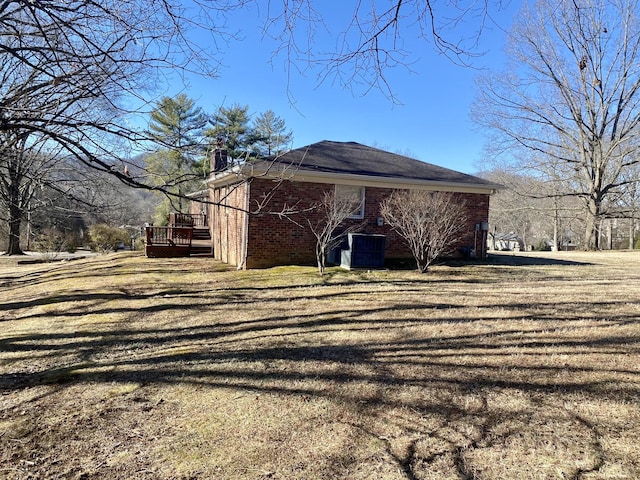 view of property exterior featuring central air condition unit, a yard, a wooden deck, and brick siding