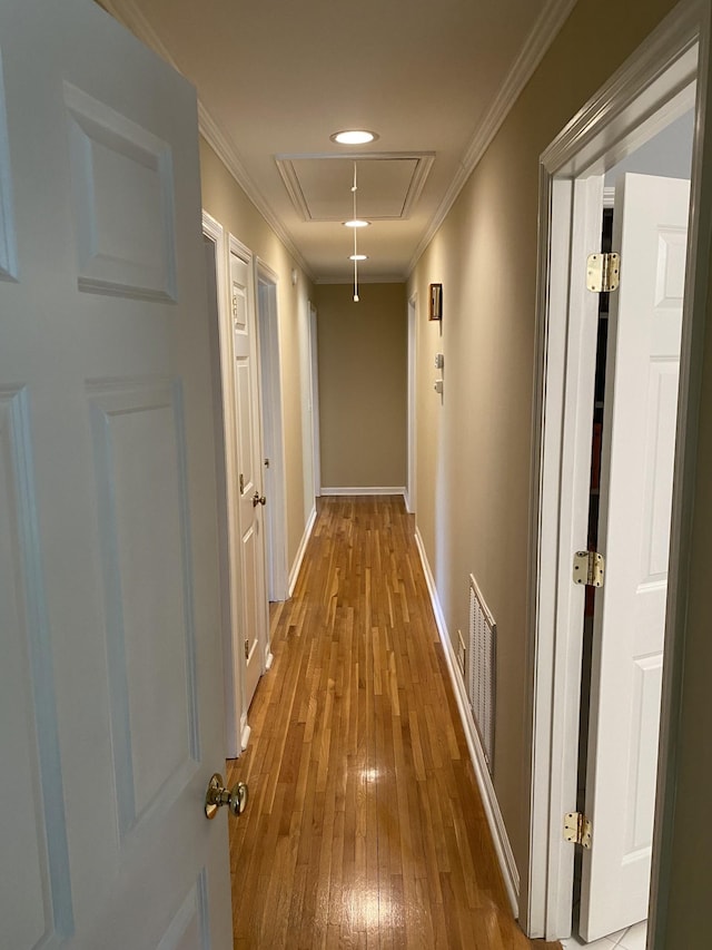 hallway featuring wood-type flooring, visible vents, attic access, ornamental molding, and baseboards