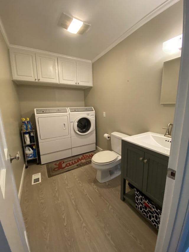 half bathroom with toilet, wood finished floors, baseboards, washer and dryer, and ornamental molding