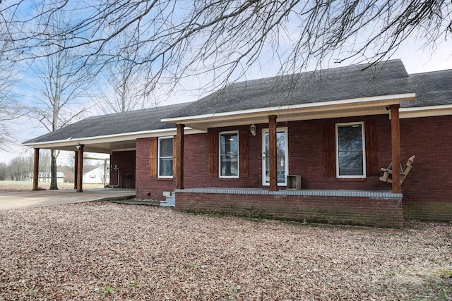 ranch-style home with brick siding, a shingled roof, covered porch, an attached carport, and driveway