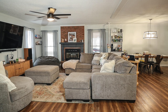 living room featuring ornamental molding, a brick fireplace, dark wood finished floors, and a textured ceiling