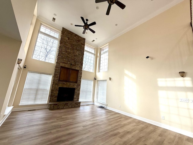 unfurnished living room with a fireplace, a towering ceiling, ornamental molding, wood finished floors, and baseboards