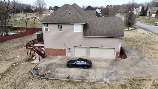 back of property featuring roof with shingles, concrete driveway, fence, a garage, and stairs
