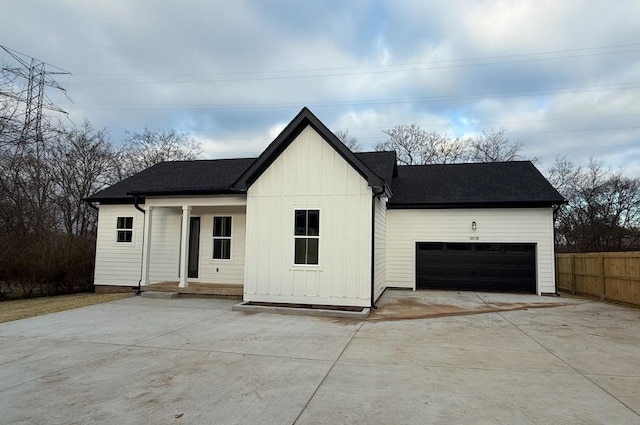 modern farmhouse featuring a garage, a shingled roof, board and batten siding, and fence