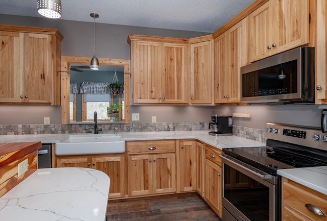 kitchen with light stone counters, decorative light fixtures, appliances with stainless steel finishes, a sink, and a textured ceiling