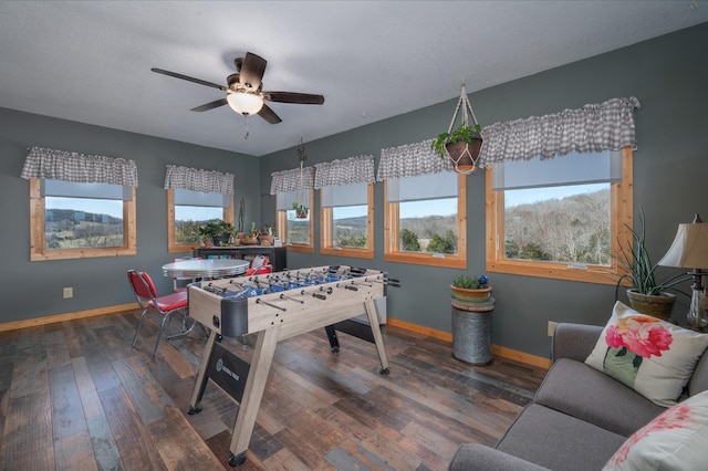 recreation room with dark wood finished floors, a textured ceiling, baseboards, and ceiling fan