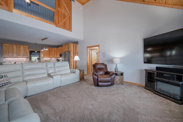 living area with baseboards, high vaulted ceiling, a glass covered fireplace, and light colored carpet