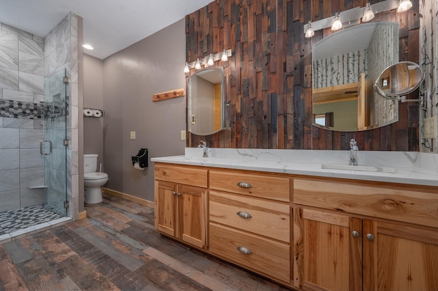 full bathroom with double vanity, toilet, wood finished floors, a shower stall, and a sink